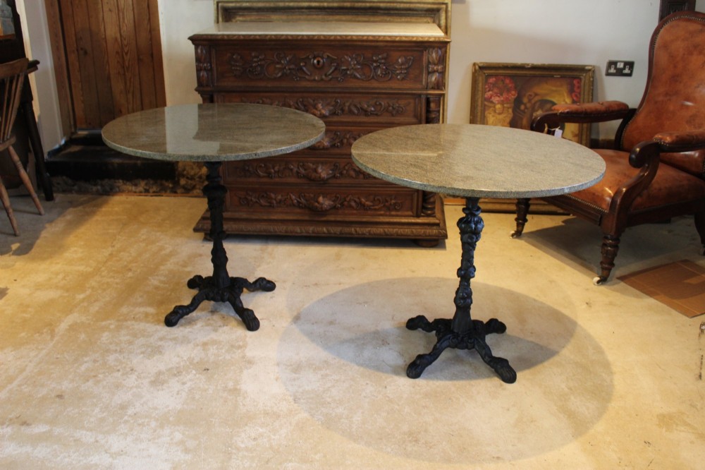 A pair of circular garden tables featuring polished grey granite tops supported by ornate black cast iron pedestal bases with claw feet.
