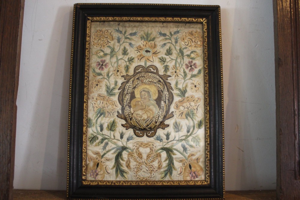 A framed 17th-century silk embroidery panel depicting a central oval medallion with a haloed figure surrounded by detailed floral scrollwork in a dark moulding frame.
