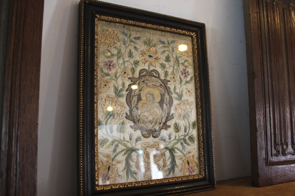 A framed 17th-century silk embroidery panel depicting a central oval medallion with a haloed figure surrounded by detailed floral scrollwork in a dark moulding frame. View II