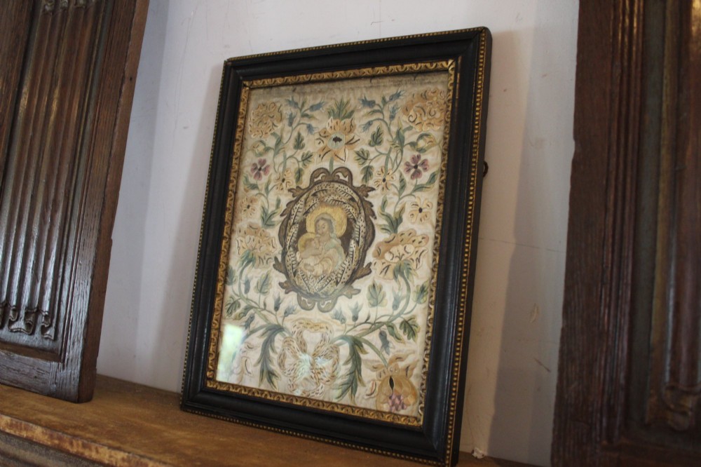 A framed 17th-century silk embroidery panel depicting a central oval medallion with a haloed figure surrounded by detailed floral scrollwork in a dark moulding frame. View III