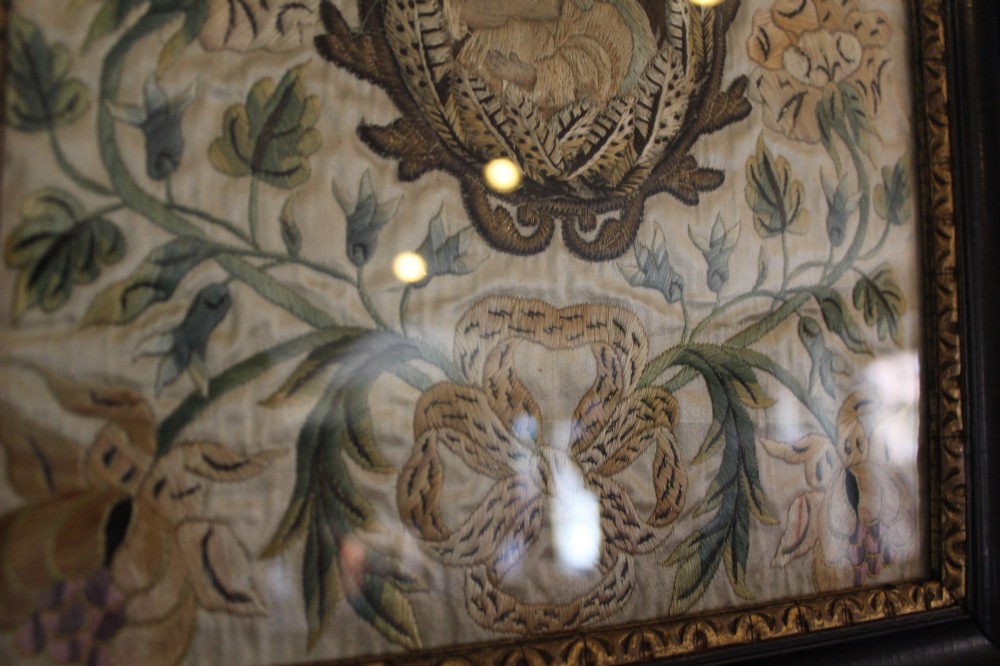A framed 17th-century silk embroidery panel depicting a central oval medallion with a haloed figure surrounded by detailed floral scrollwork in a dark moulding frame. View V