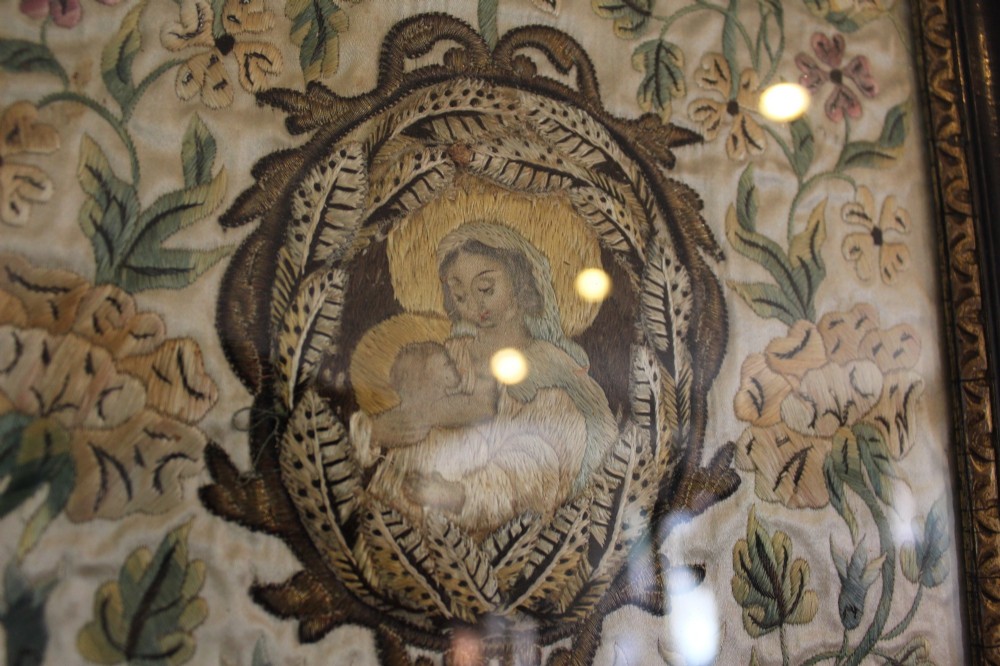 A framed 17th-century silk embroidery panel depicting a central oval medallion with a haloed figure surrounded by detailed floral scrollwork in a dark moulding frame. View VI