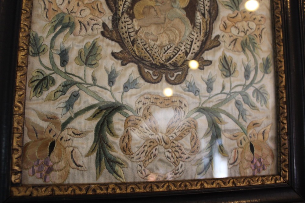 A framed 17th-century silk embroidery panel depicting a central oval medallion with a haloed figure surrounded by detailed floral scrollwork in a dark moulding frame. View IX