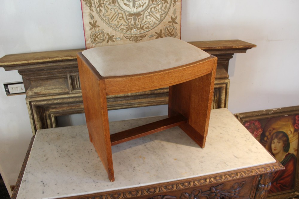 An oak stool featuring solid slab side supports, a central connecting stretcher, and a concave upholstered fabric seat cushion. View IV