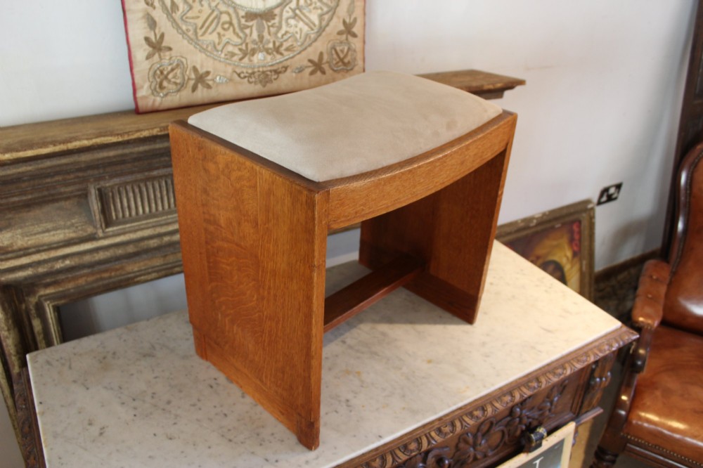 An oak stool featuring solid slab side supports, a central connecting stretcher, and a concave upholstered fabric seat cushion. View VIII