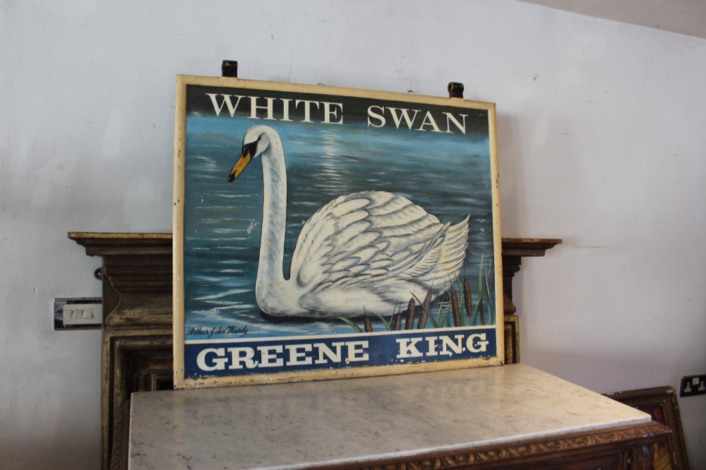 A double-sided rectangular painted metal pub sign depicting a white swan floating on blue water with White Swan text above and Greene King text below.