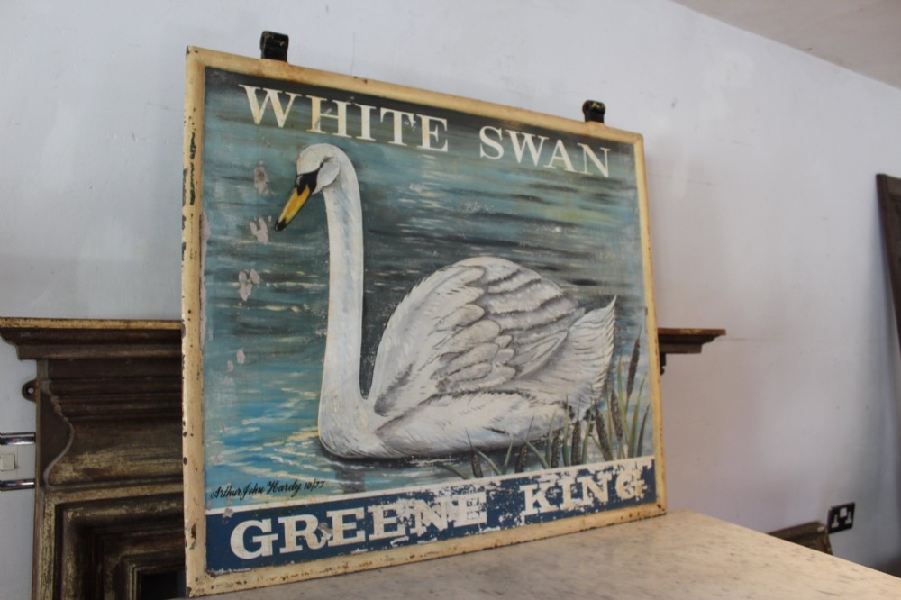 A double-sided rectangular painted metal pub sign depicting a white swan floating on blue water with White Swan text above and Greene King text below. View VI