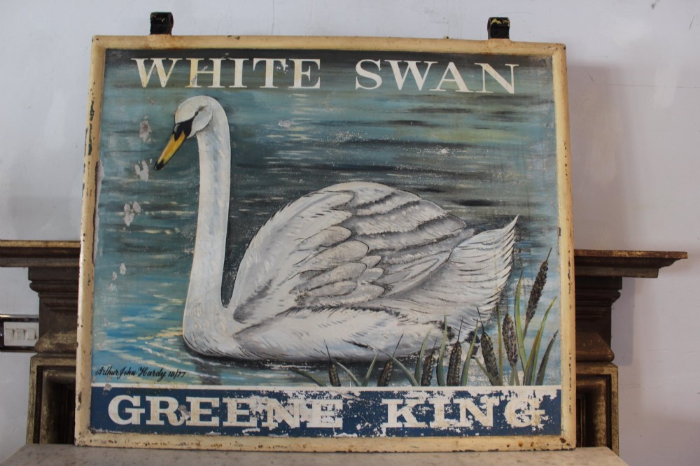 A double-sided rectangular painted metal pub sign depicting a white swan floating on blue water with White Swan text above and Greene King text below. View IX