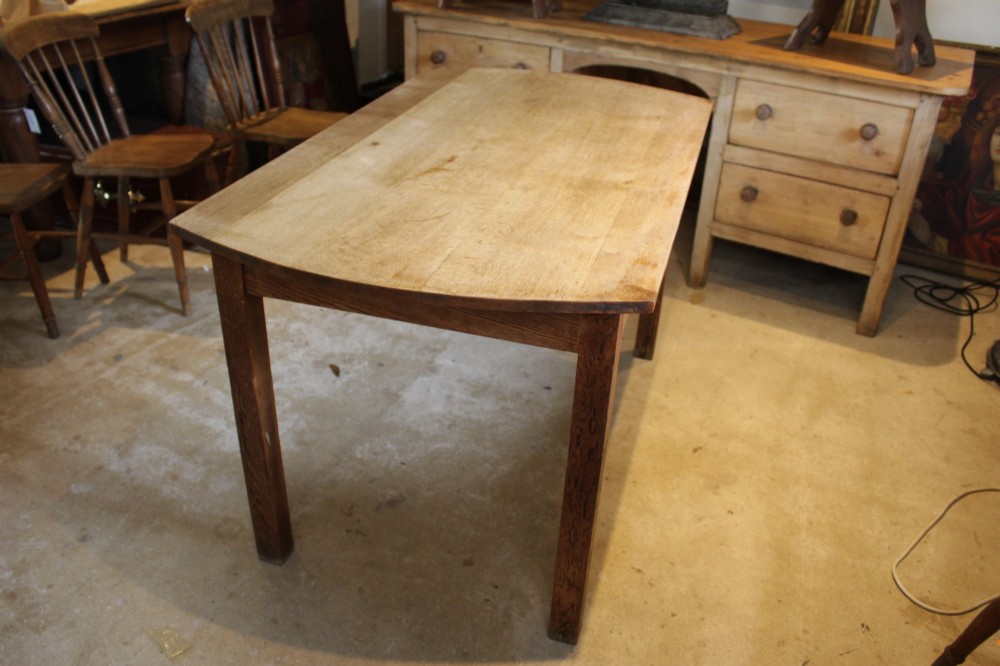 An Edwardian light oak dining table featuring a rectangular top with subtly curved short ends, supported by four straight square legs. View X