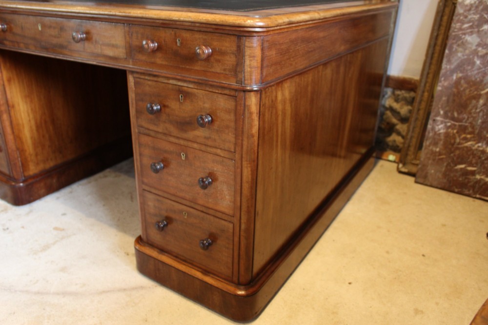 An early Victorian mahogany partners desk featuring a black leather writing top, twin pedestals with multiple drawers, and turned wooden handles. View V