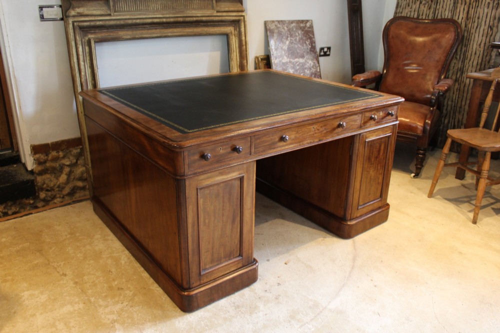 An early Victorian mahogany partners desk featuring a black leather writing top, twin pedestals with multiple drawers, and turned wooden handles. View VI