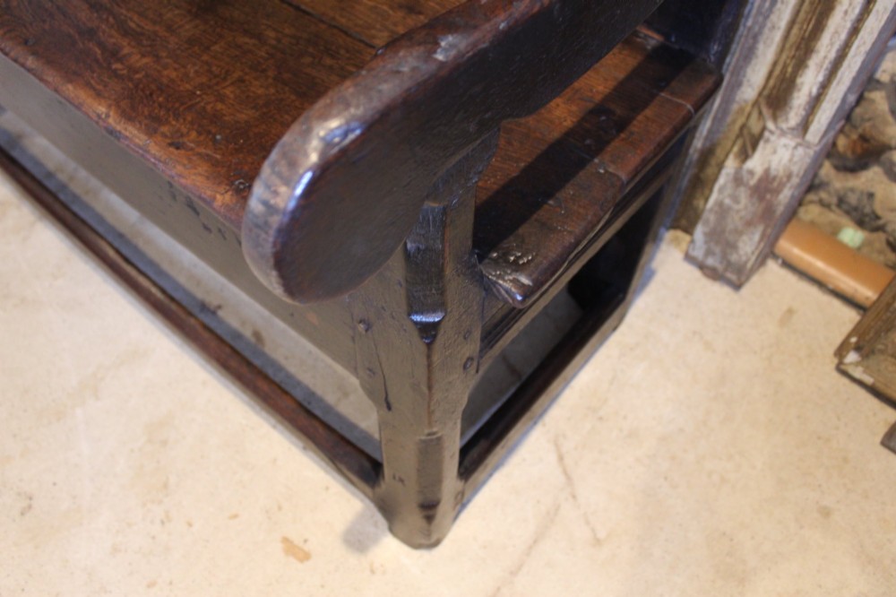 A dark oak 17th-century style settle bench with a three-panel backrest, shaped armrests, and wooden stretchers. View II