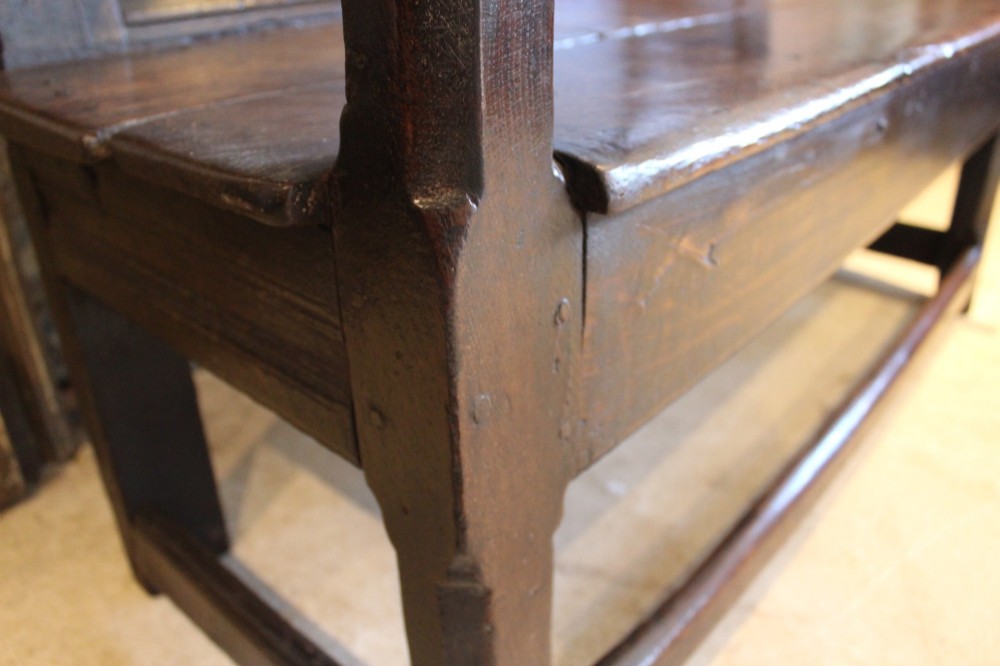 A dark oak 17th-century style settle bench with a three-panel backrest, shaped armrests, and wooden stretchers. View IX