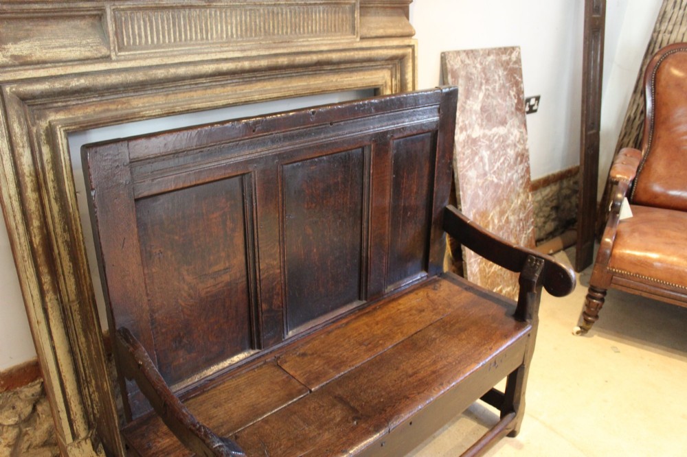 A dark oak 17th-century style settle bench with a three-panel backrest, shaped armrests, and wooden stretchers. View XI
