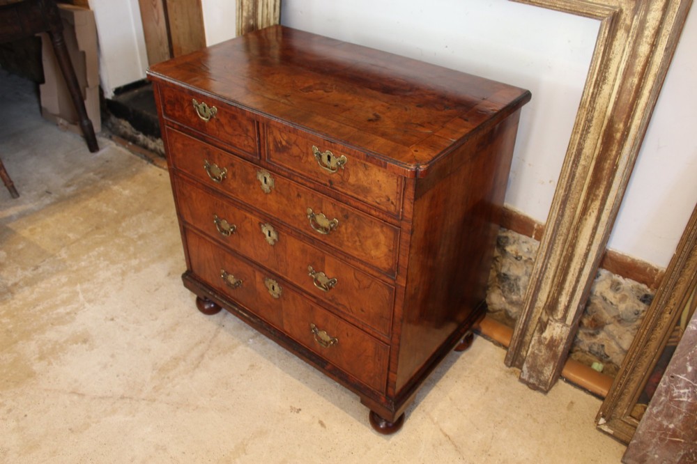 A compact George II walnut chest of drawers featuring decorative brass handles, crossbanded veneer top, and turned bun feet.