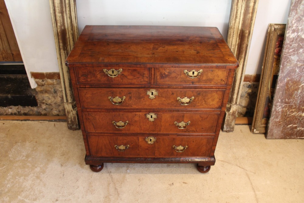 A compact George II walnut chest of drawers featuring decorative brass handles, crossbanded veneer top, and turned bun feet. View II