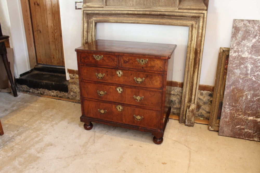 A compact George II walnut chest of drawers featuring decorative brass handles, crossbanded veneer top, and turned bun feet. View VI