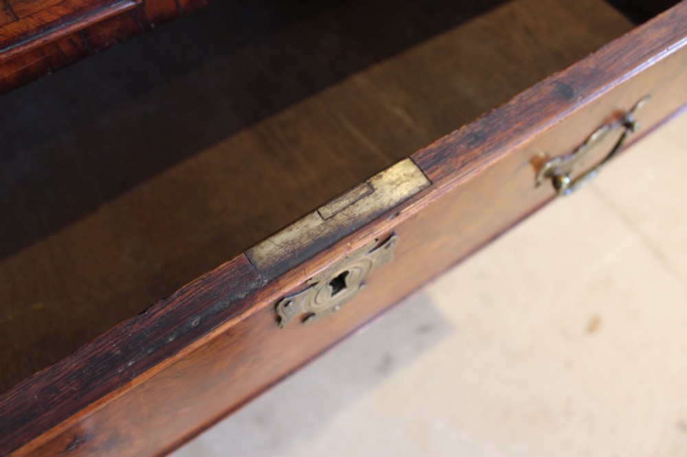 A compact George II walnut chest of drawers featuring decorative brass handles, crossbanded veneer top, and turned bun feet. View VIII