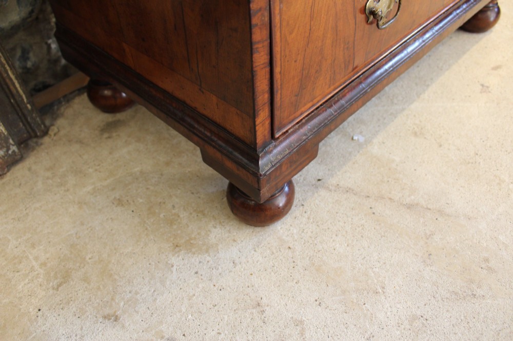 A compact George II walnut chest of drawers featuring decorative brass handles, crossbanded veneer top, and turned bun feet. View X
