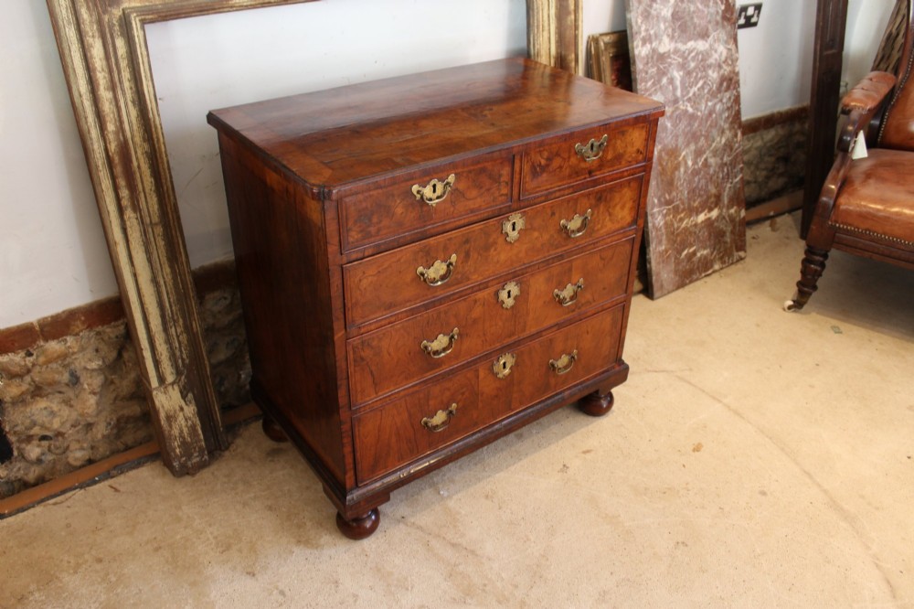 A compact George II walnut chest of drawers featuring decorative brass handles, crossbanded veneer top, and turned bun feet. View XII