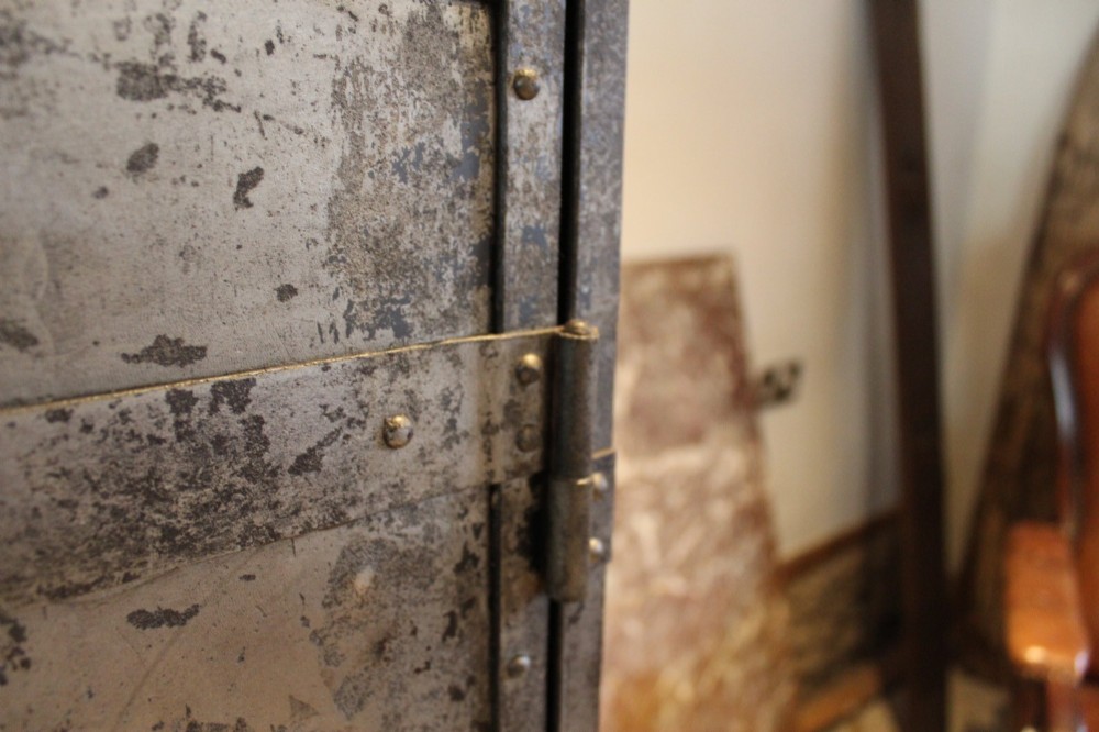 A tall, narrow Victorian industrial metal cupboard featuring a single door with a dark grey patinated surface, riveted frame, brass number plaque, and latch handle. View III