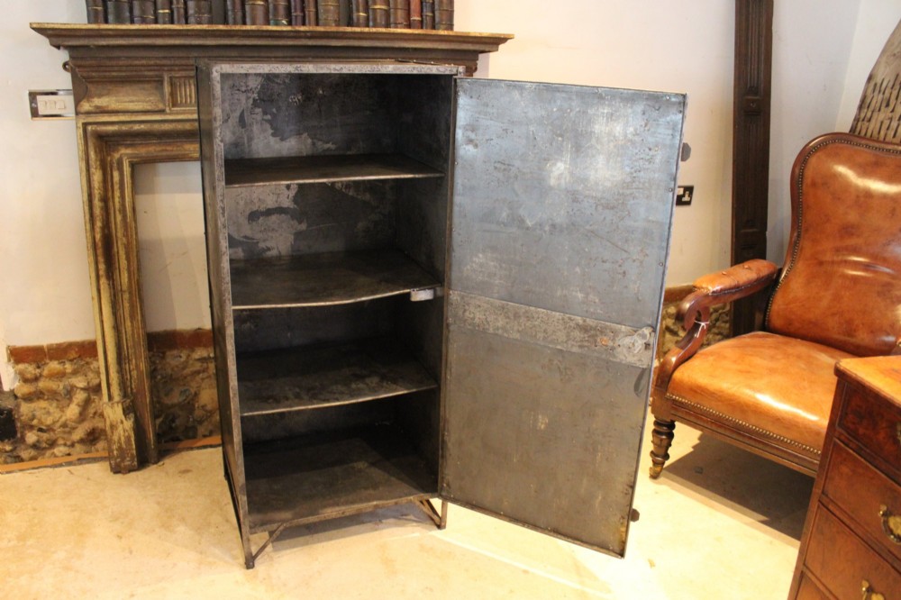 A tall, narrow Victorian industrial metal cupboard featuring a single door with a dark grey patinated surface, riveted frame, brass number plaque, and latch handle. View IV