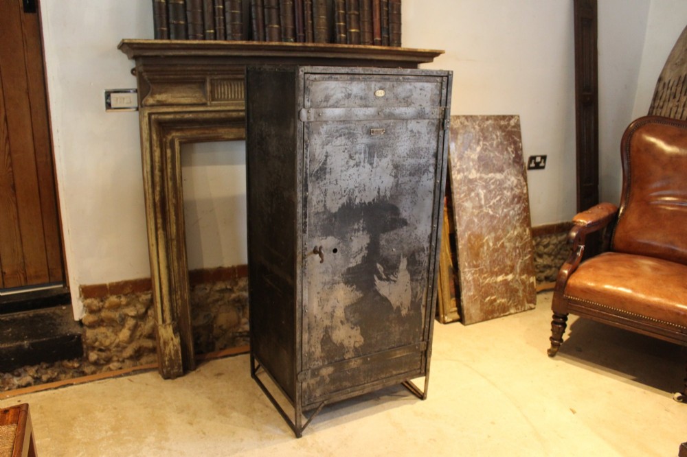 A tall, narrow Victorian industrial metal cupboard featuring a single door with a dark grey patinated surface, riveted frame, brass number plaque, and latch handle. View VI