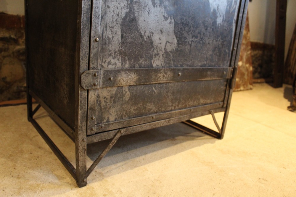 A tall, narrow Victorian industrial metal cupboard featuring a single door with a dark grey patinated surface, riveted frame, brass number plaque, and latch handle. View IX