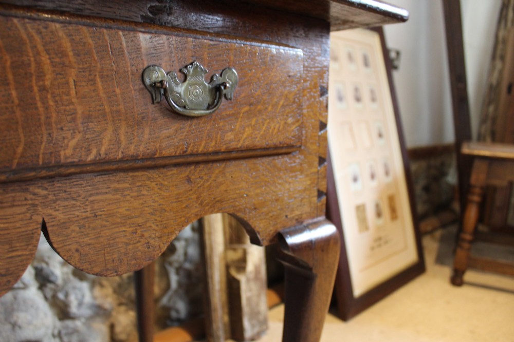 A George II oak lowboy table featuring a single drawer with brass handles, a scalloped apron, and slender cabriole legs ending in pad feet. View XI