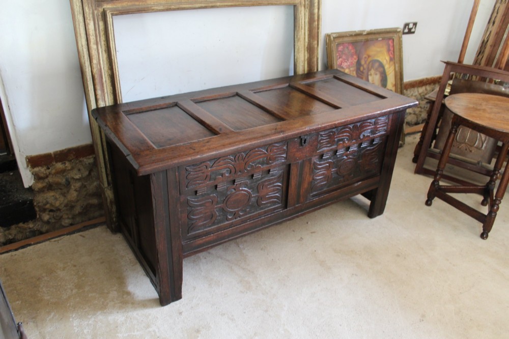 A 17th-century dark oak coffer featuring carved front panels and a four-panel hinged lid.