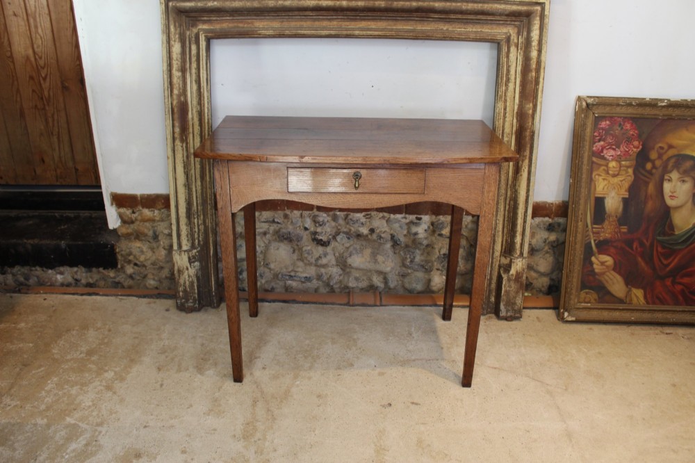 A George III country oak side table featuring a single frieze drawer with a brass drop handle, a shaped apron, and four straight legs.