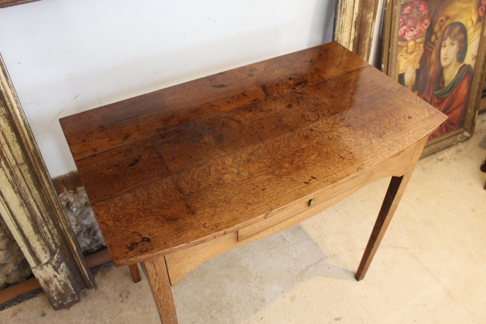 A George III country oak side table featuring a single frieze drawer with a brass drop handle, a shaped apron, and four straight legs. View IV