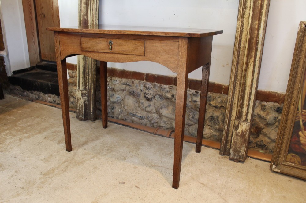 A George III country oak side table featuring a single frieze drawer with a brass drop handle, a shaped apron, and four straight legs. View VII