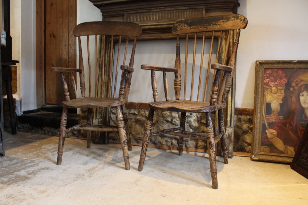 A pair of late 19th-century Windsor armchairs featuring shaped elm seats, spindle backs, turned legs, and distressed dark brown patinated finish.