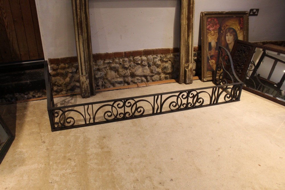 A large dark steel fire fender featuring decorative scrolling ironwork along the front and side returns.