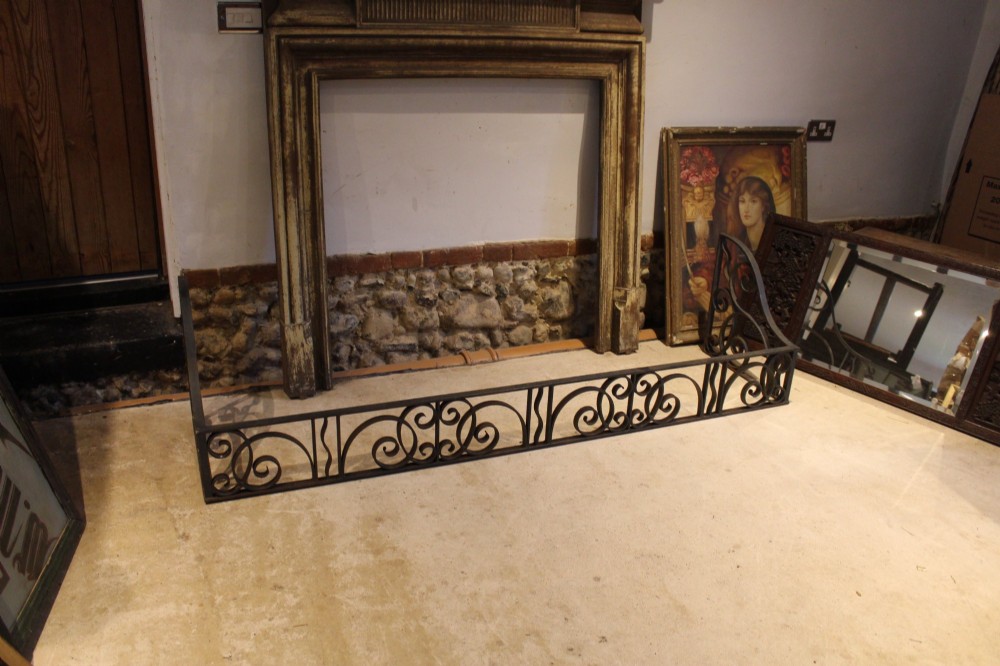 A large dark steel fire fender featuring decorative scrolling ironwork along the front and side returns. View III