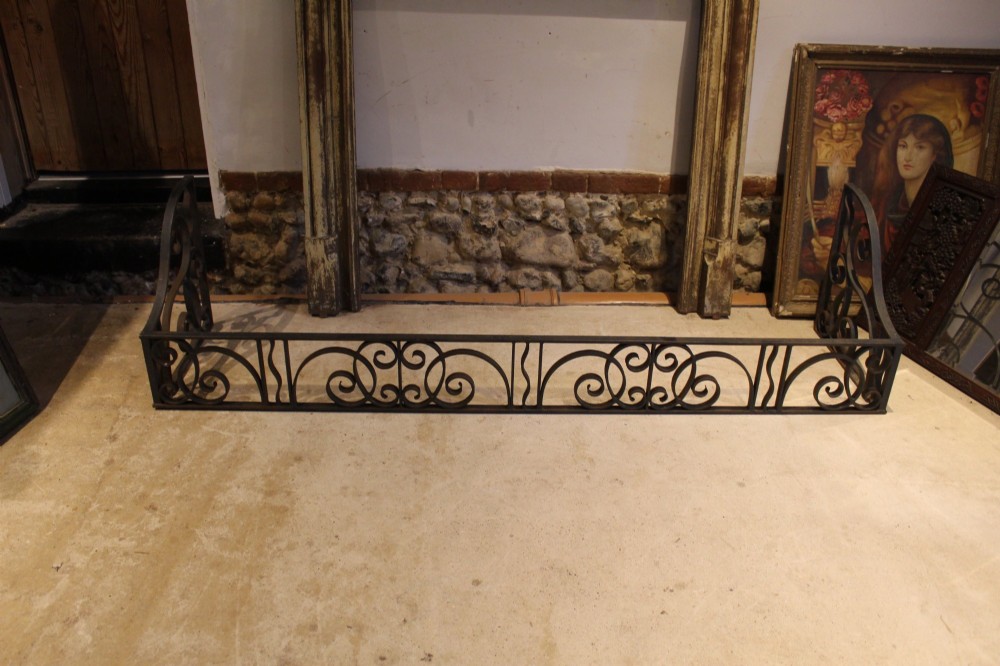 A large dark steel fire fender featuring decorative scrolling ironwork along the front and side returns. View VII