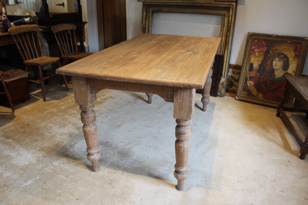 An Edwardian rectangular pitch pine dining table with a thick plank top and four stout turned legs. View IV