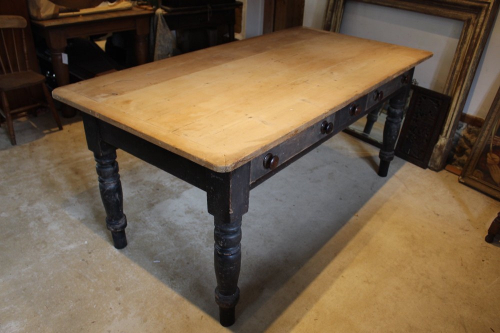 A 19th-century pine farmhouse dining table featuring a natural scrubbed wooden top, frieze drawers with round wooden knobs, and turned dark painted legs.