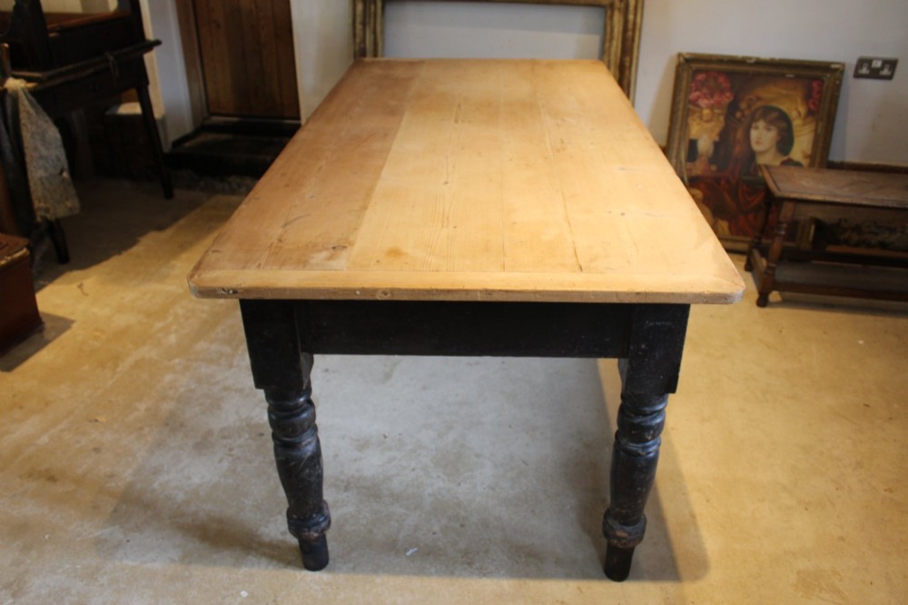 A 19th-century pine farmhouse dining table featuring a natural scrubbed wooden top, frieze drawers with round wooden knobs, and turned dark painted legs. View XII