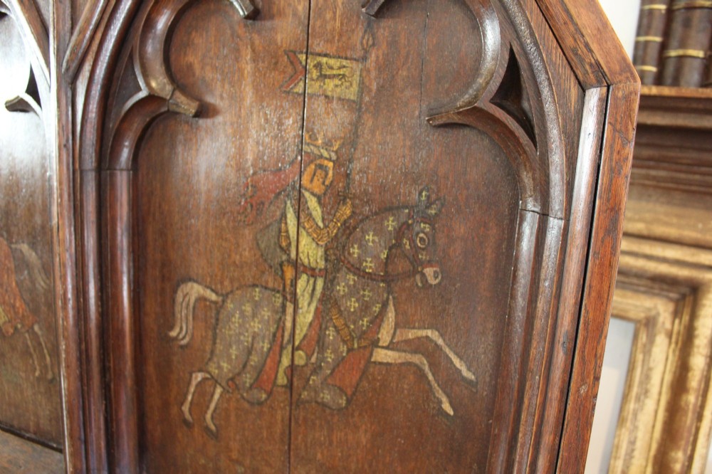 A pair of arched dark oak architectural panels featuring carved Gothic tracery and polychrome paintings of mounted medieval knights and heraldic shields. View III