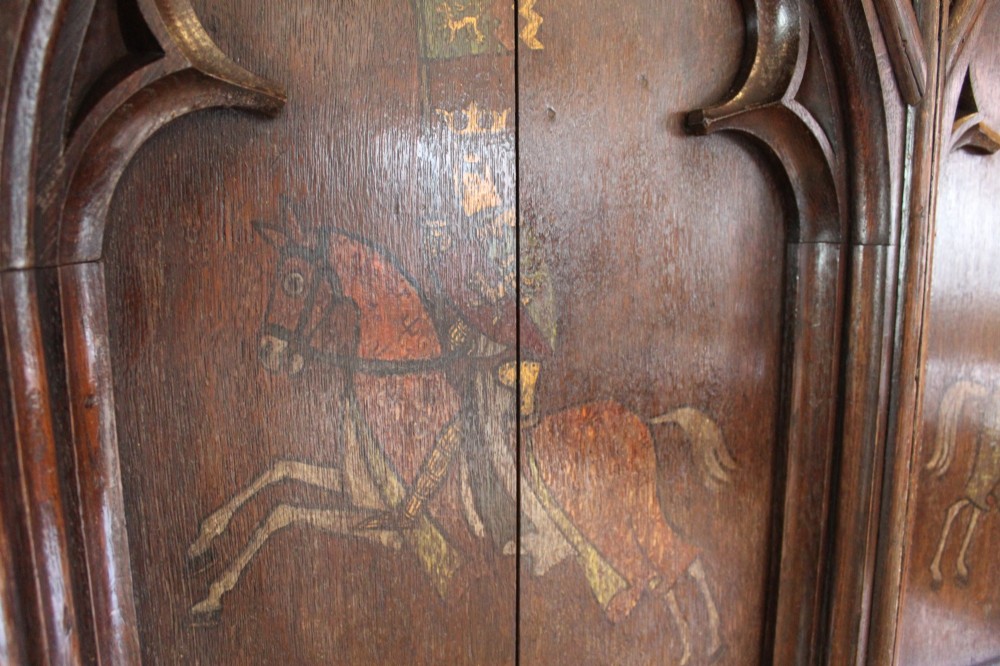 A pair of arched dark oak architectural panels featuring carved Gothic tracery and polychrome paintings of mounted medieval knights and heraldic shields. View IX