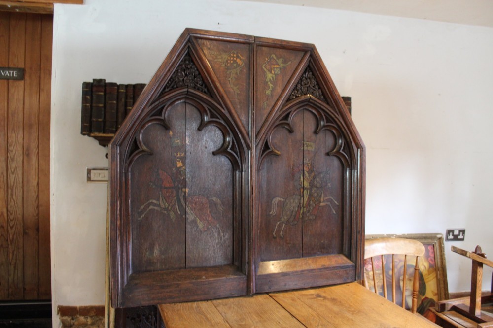 A pair of arched dark oak architectural panels featuring carved Gothic tracery and polychrome paintings of mounted medieval knights and heraldic shields. View XII