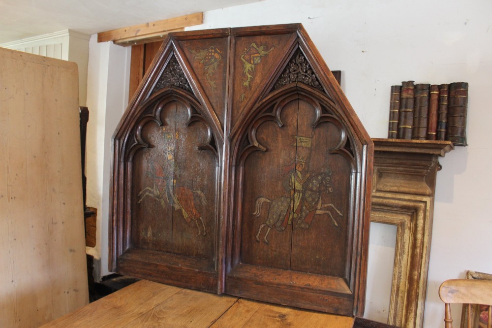 A pair of arched dark oak architectural panels featuring carved Gothic tracery and polychrome paintings of mounted medieval knights and heraldic shields. View XIII
