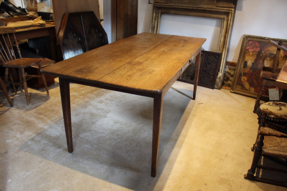 An antique French oak refectory dining table featuring a solid two-plank top, a side frieze drawer, and square tapered legs.