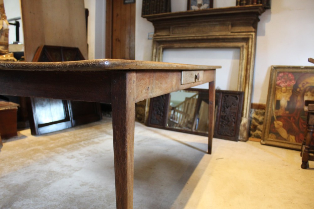 An antique French oak refectory dining table featuring a solid two-plank top, a side frieze drawer, and square tapered legs. View III