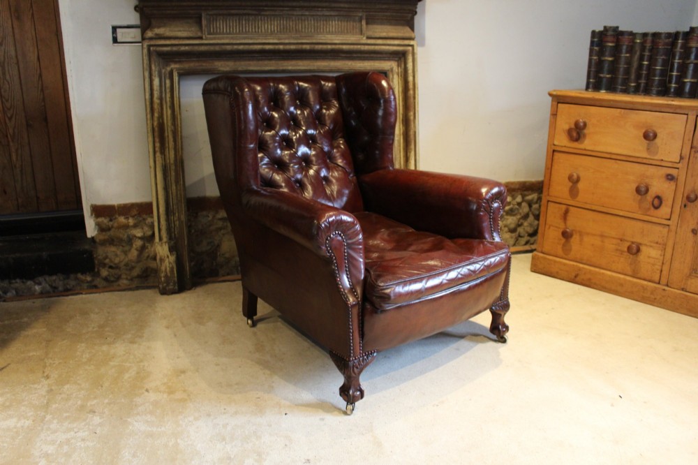A late Victorian deep-buttoned chestnut brown leather wingback armchair featuring brass studding, carved front legs with ball-and-claw feet, and metal castors.