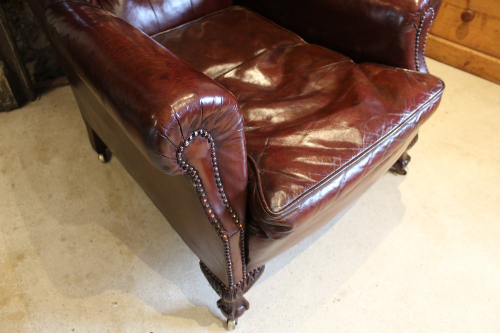 A late Victorian deep-buttoned chestnut brown leather wingback armchair featuring brass studding, carved front legs with ball-and-claw feet, and metal castors. View II