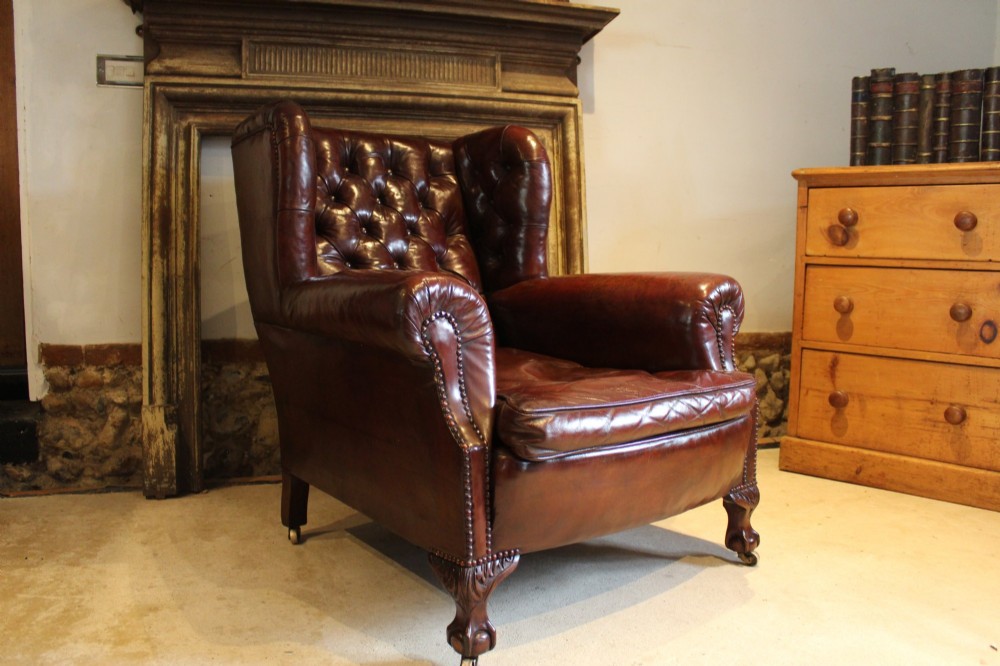 A late Victorian deep-buttoned chestnut brown leather wingback armchair featuring brass studding, carved front legs with ball-and-claw feet, and metal castors. View III