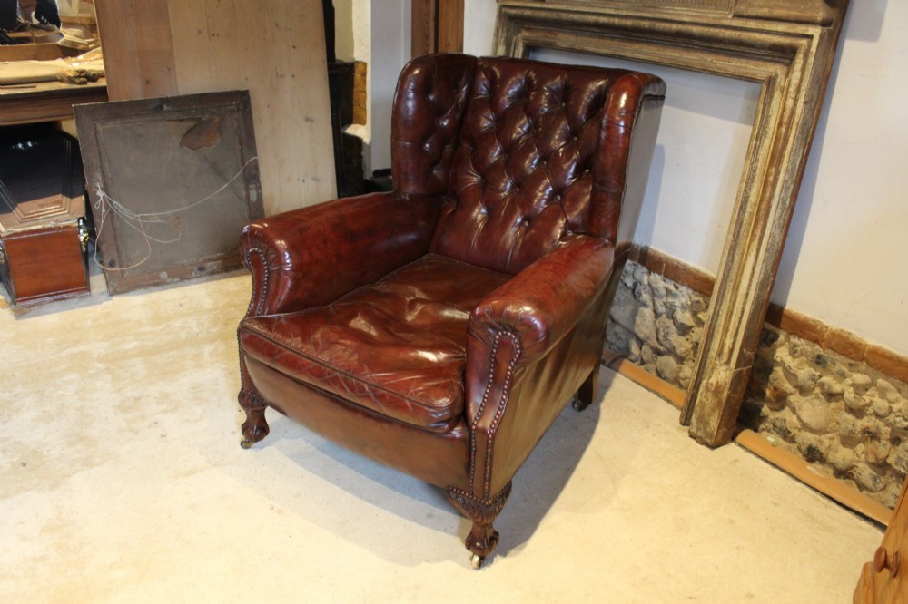 A late Victorian deep-buttoned chestnut brown leather wingback armchair featuring brass studding, carved front legs with ball-and-claw feet, and metal castors. View IV